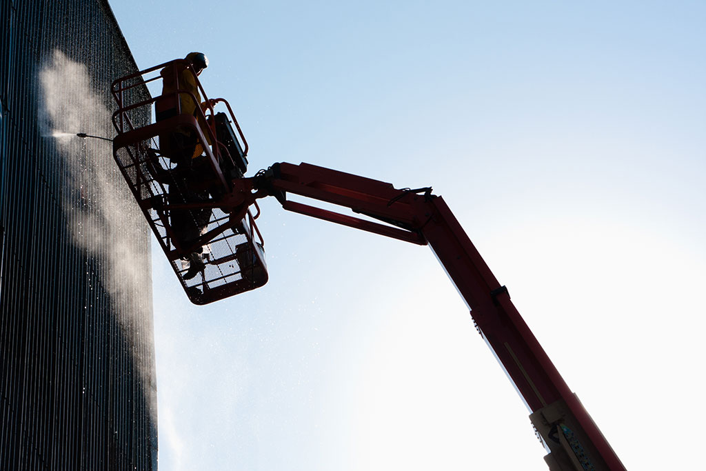 worker-high-up-in-cherry-picker-power-washing-high-industrial-building